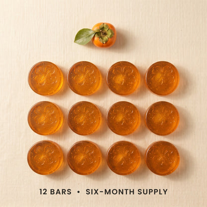 Twelve Kakiyu persimmon soap bars in a grid on cream linen, a six-month supply