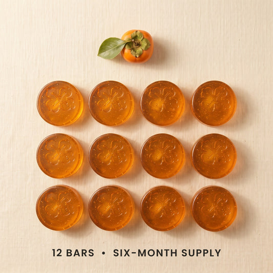 Twelve Kakiyu persimmon soap bars in a grid on cream linen, a six-month supply